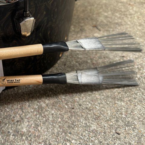 Two Vater Wire Tap wood brushes with wire bristles, held in a white clip on the floor tom.
