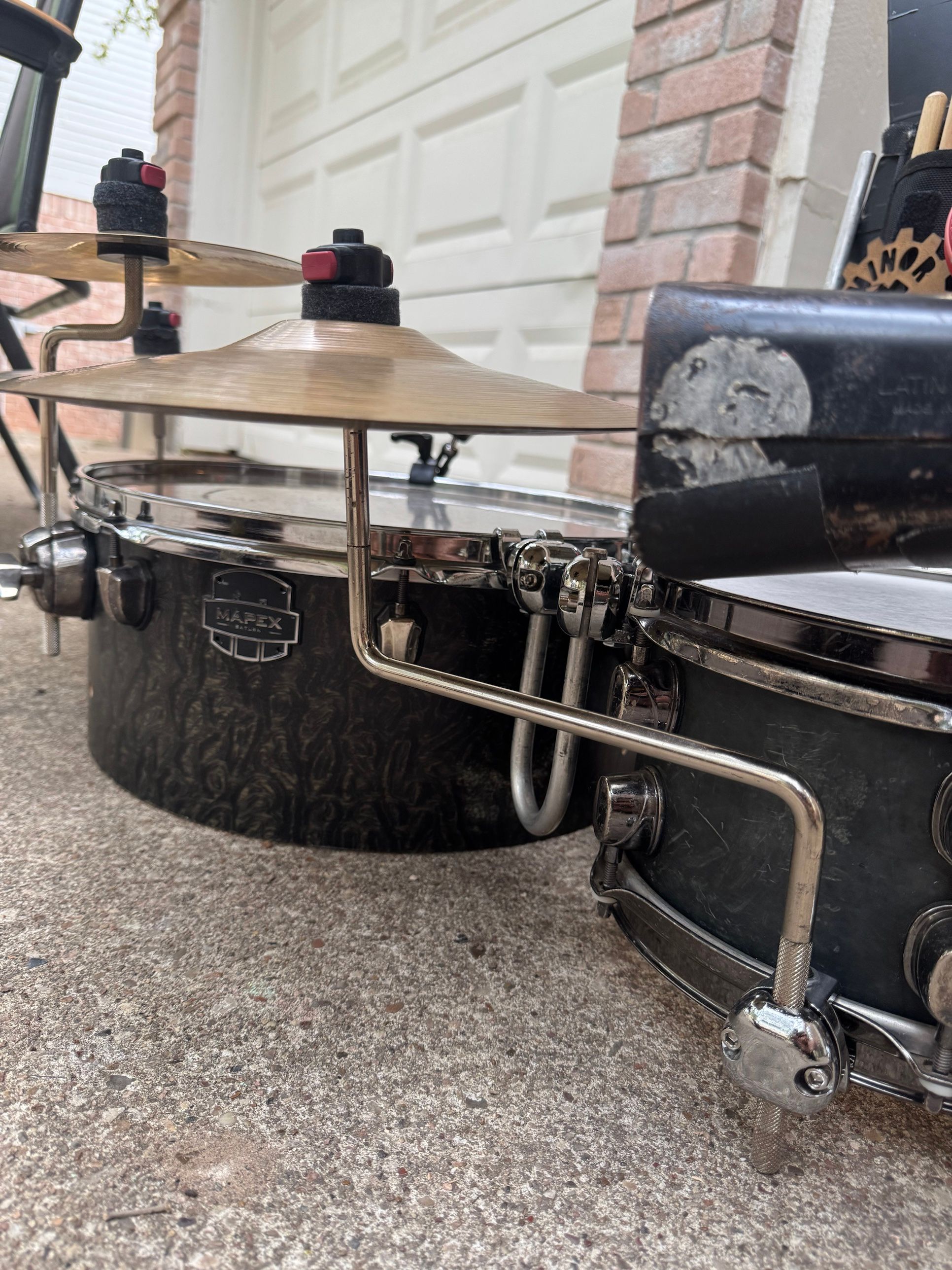 Side view of the floor tom and the snare, with a long bent rod running from a clamp at the bottom of the snare up to a cymbal between the two drums.
