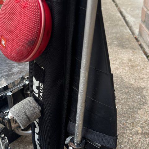 A black ProMark stick bag on the harness, holding sticks and mallets, with a red speaker clipped to it.