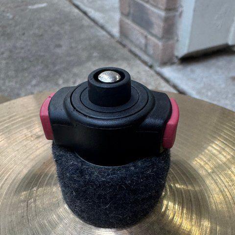 A black quick-set cymbal nut with red release tabs and a felt sleeve, on a cymbal bell.