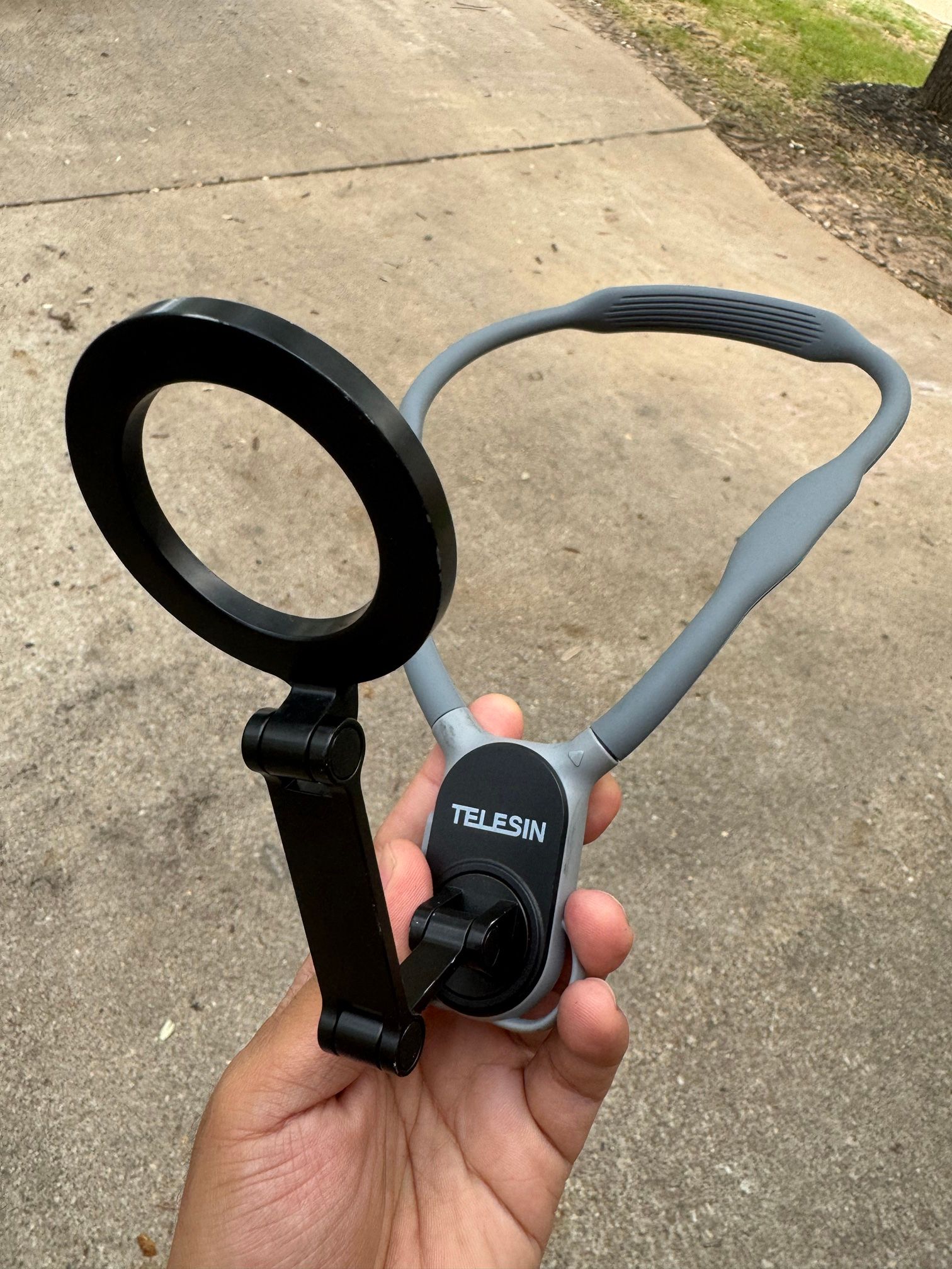 A grey TELESIN neck mount with a black magnetic phone ring, held in a hand.